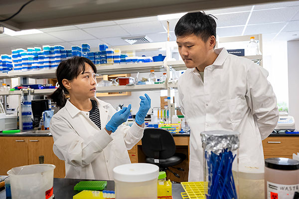 A young woman and a young man in a biochemistry lab, surrounded by lab equipment.