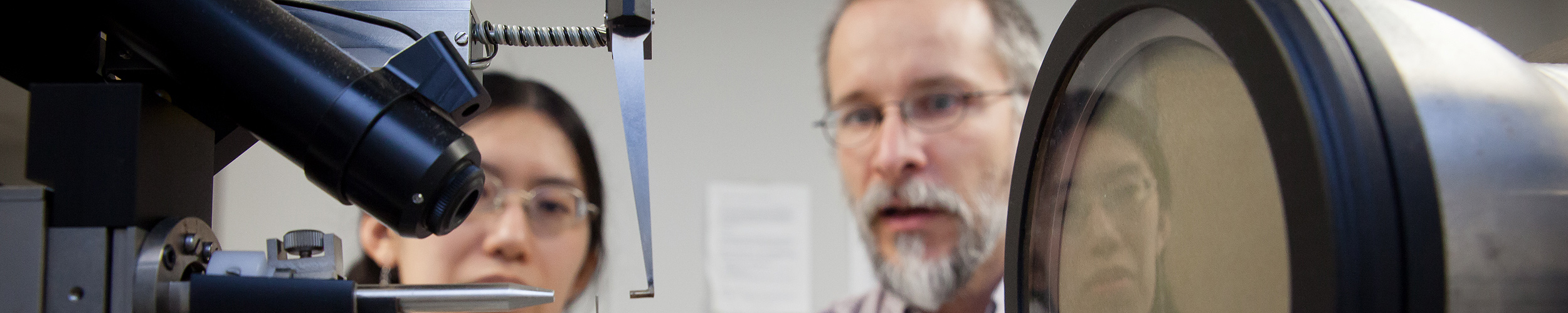 A male professor and female student in soft focus, looking at lab equipment in the foreground.